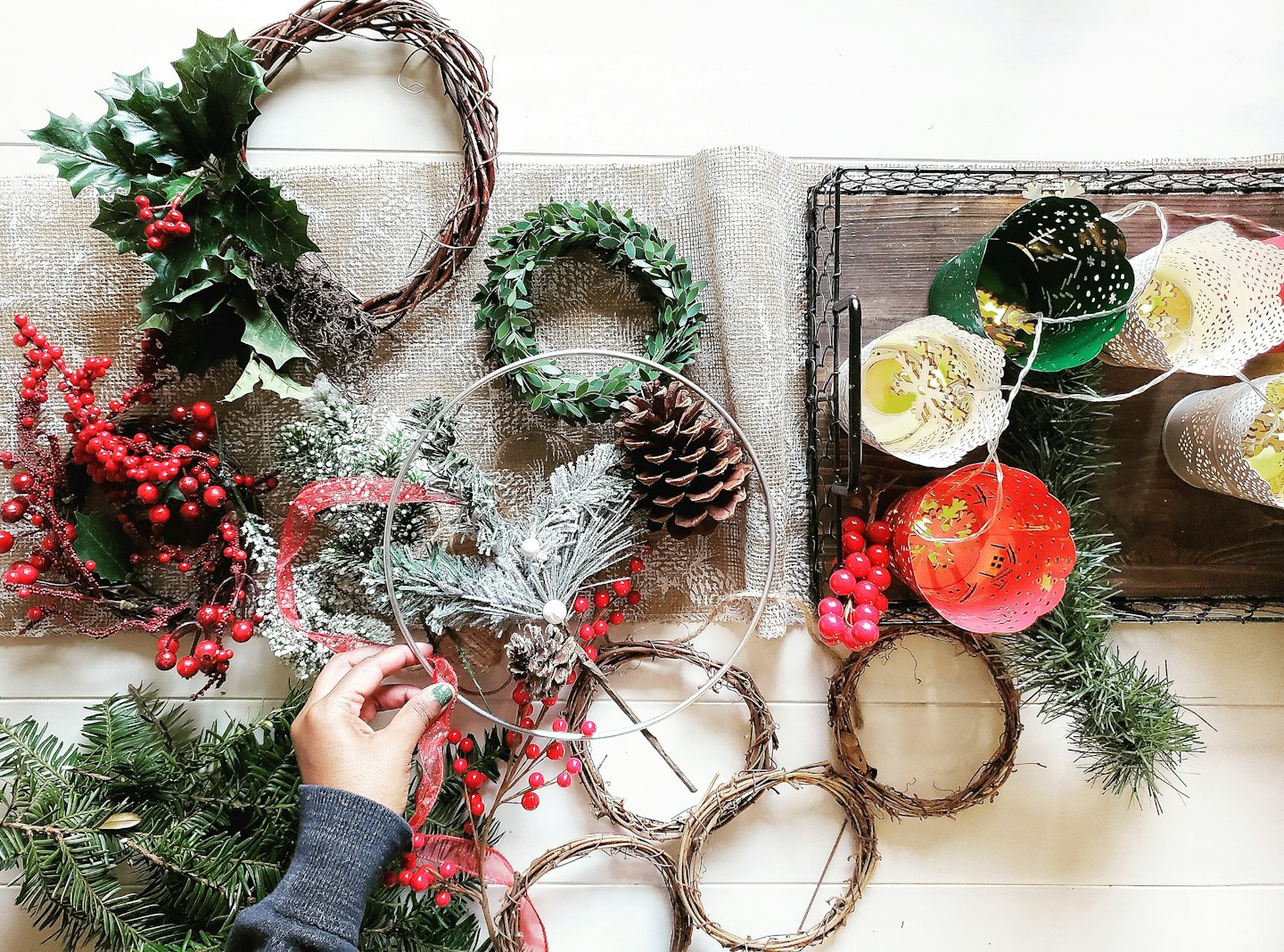 Hands arranging festive holiday decorations on a wooden table.