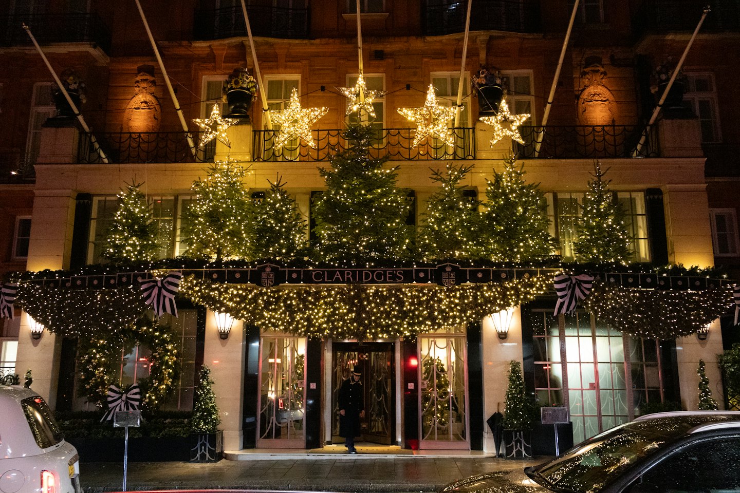 A doorman stands at the decorated hotel entrance at night.